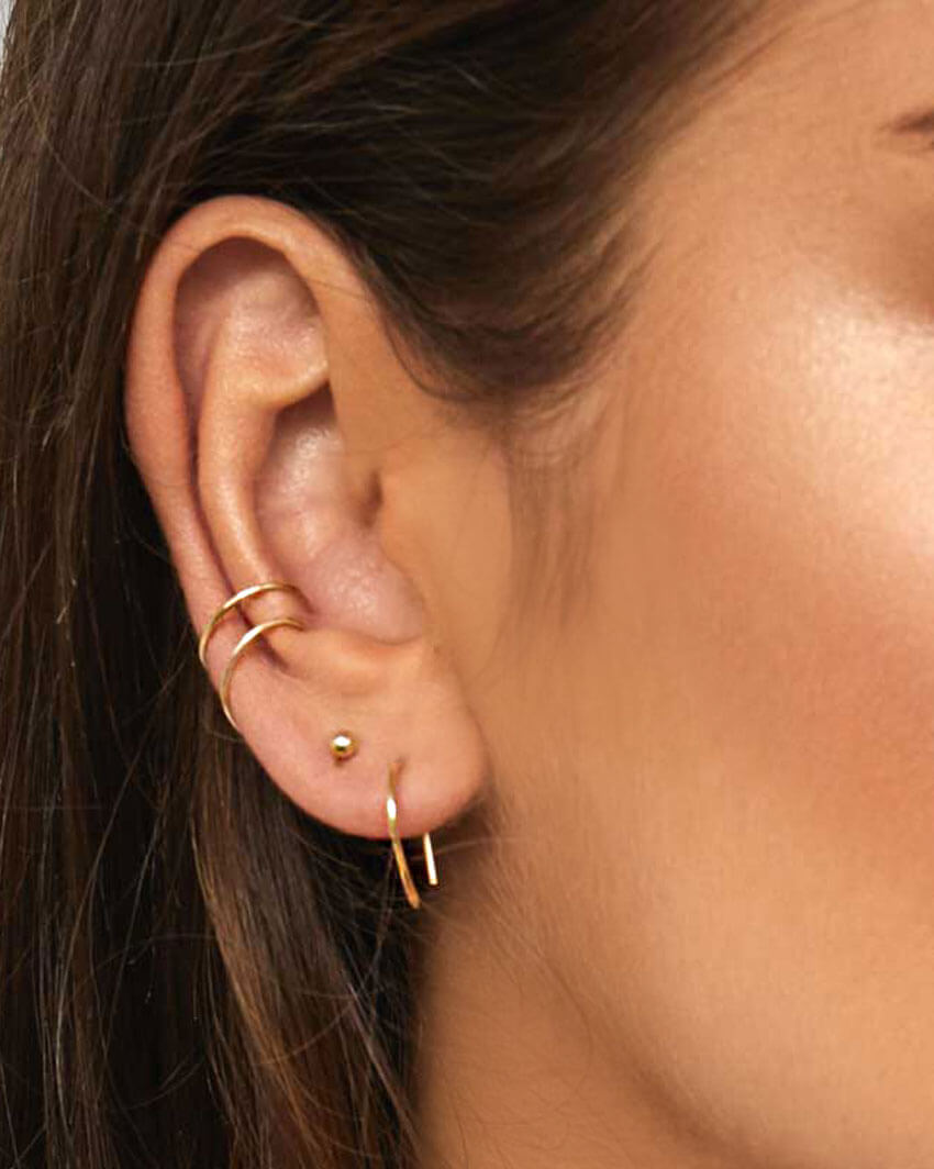 Model wears arc earrings gold and fine ear cuffs in multiple piercings